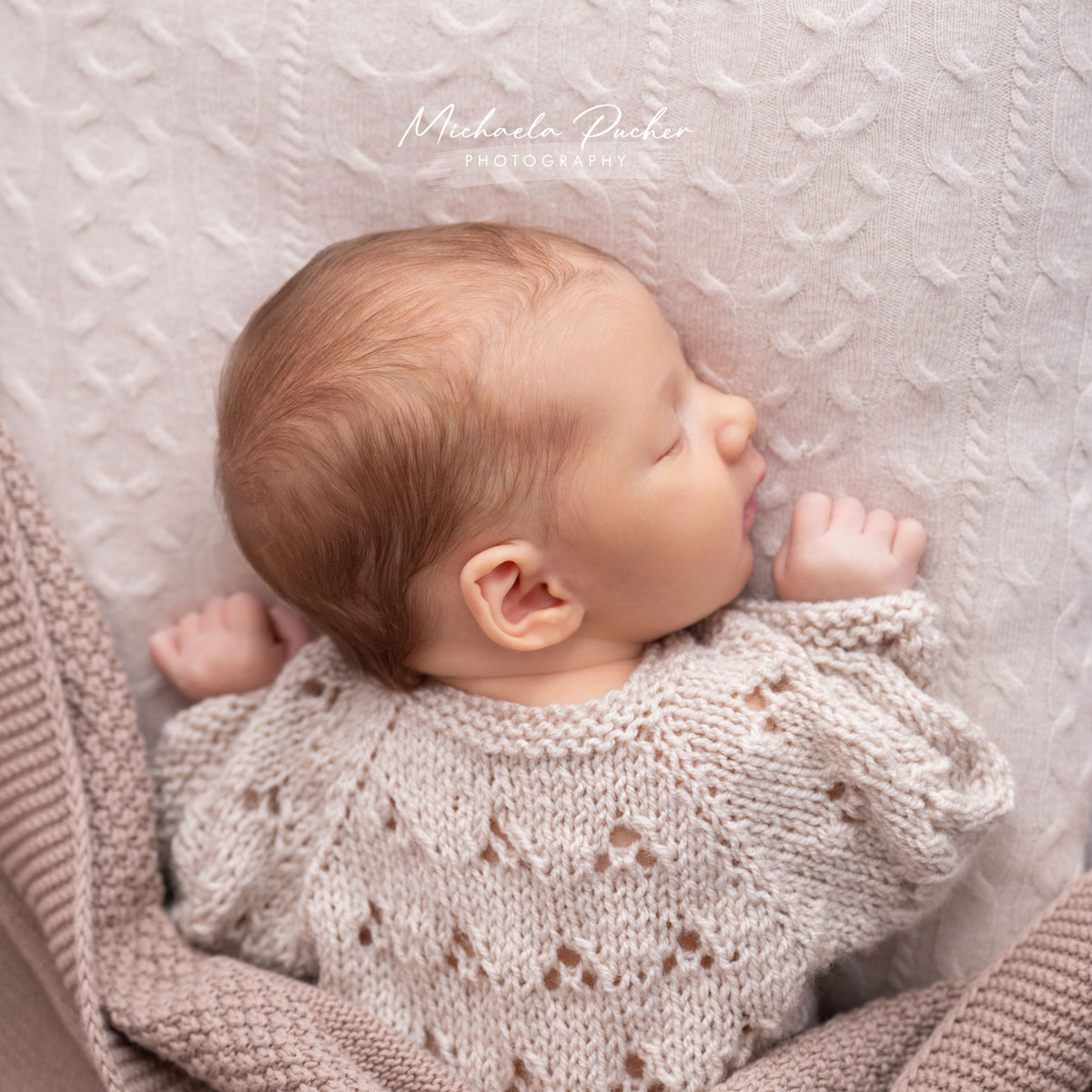 Schlafendes Neugeborenes in einem gestrickten Creme-Pullover, eingerahmt von weichen Decken in Naturtönen.